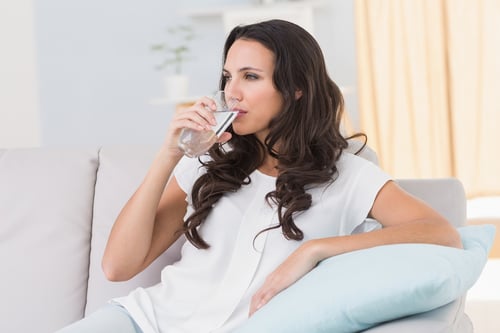 Pretty brunette drinking water on couch at home in the living room