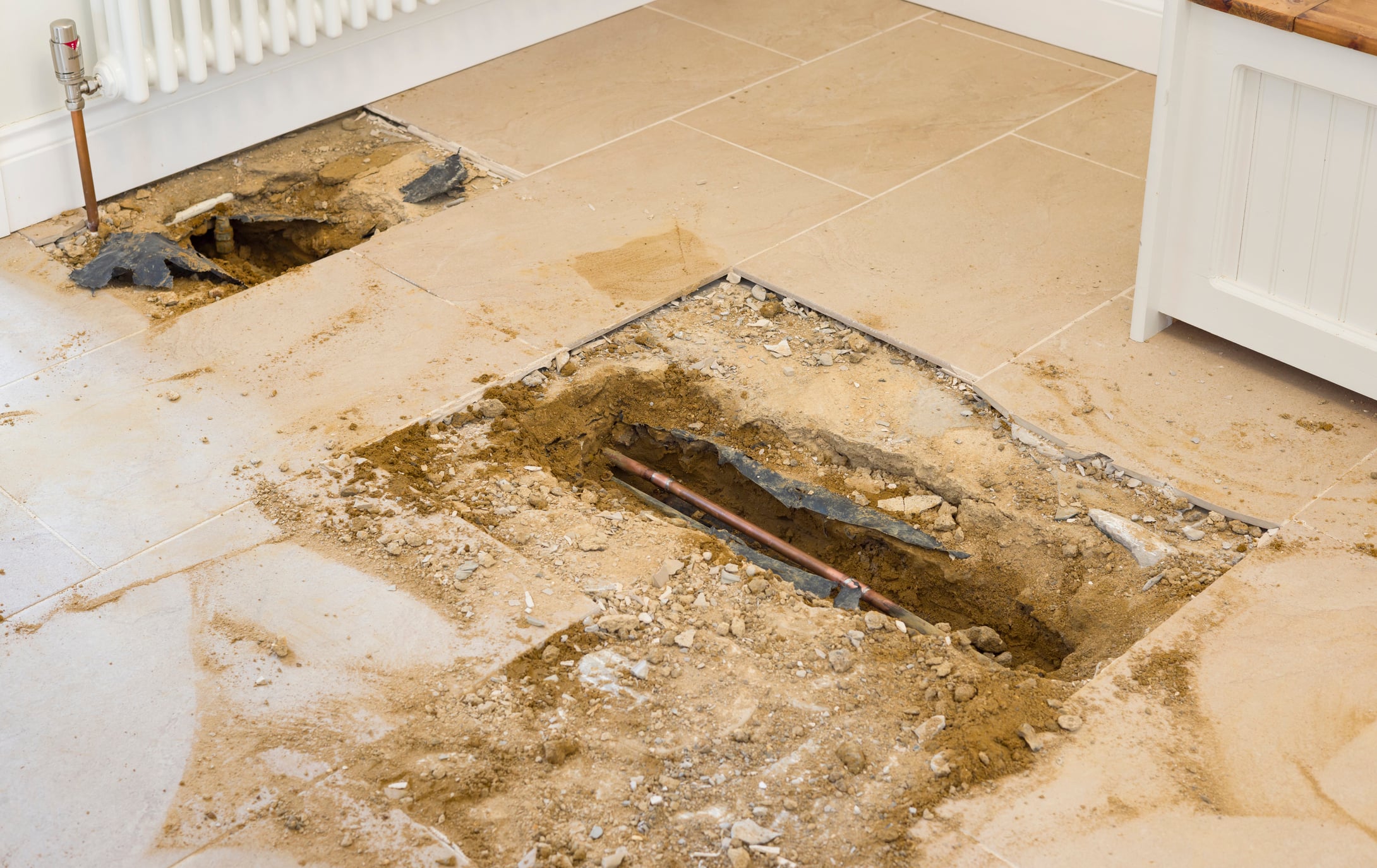 Exposed copper plumbing pipe beneath a tiled floor during slab leak detection and repair.