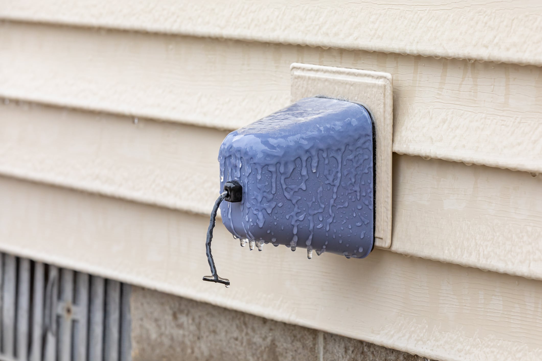 Close-up of an insulated outdoor water spigot cover coated in ice, protecting exterior plumbing pipes from freezing temperatures.