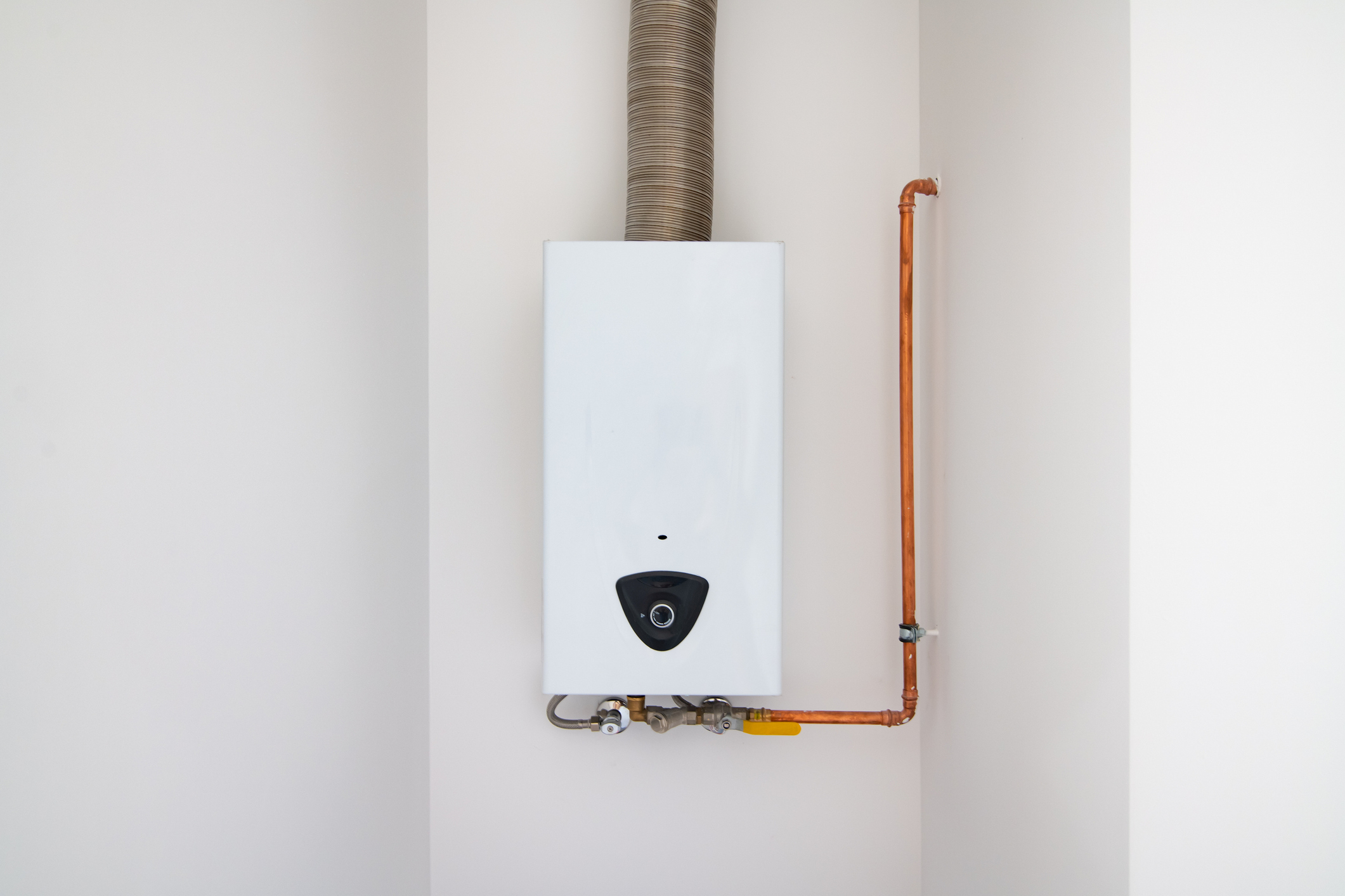 Wall-mounted tankless water heater with exposed copper piping and a vent pipe in a clean, modern interior.
