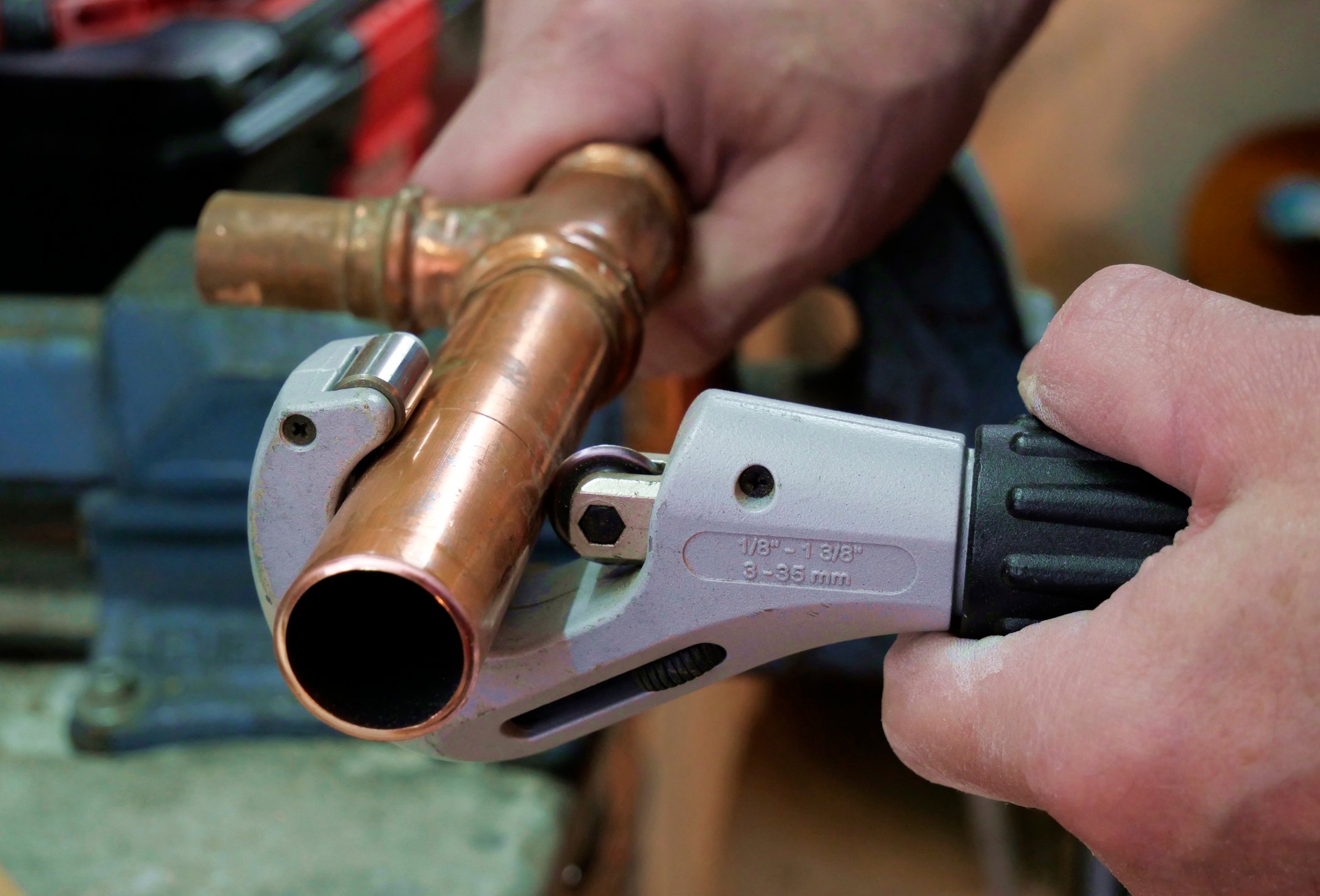 Plumber cuts copper pipe with pipe cutter
